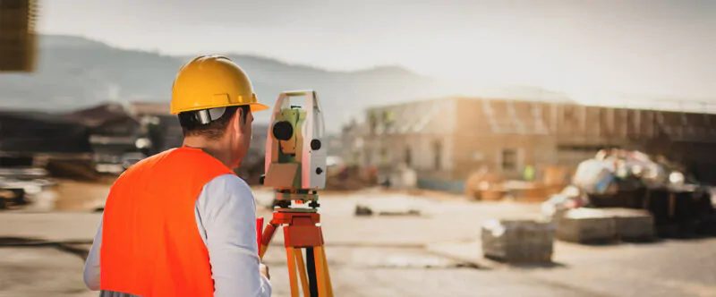 Topógrafo com estação total realizando locação topográfica em canteiro de obras
